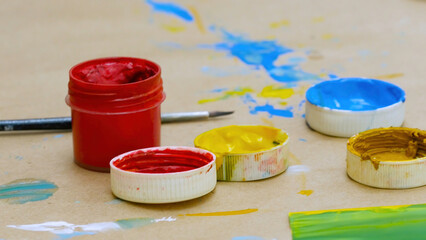 Open small paint jar of red color standing on a table with paint stains and a brush, art and...