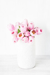 Bouquet of pink tulips in white ceramic vase on white table. Copy space