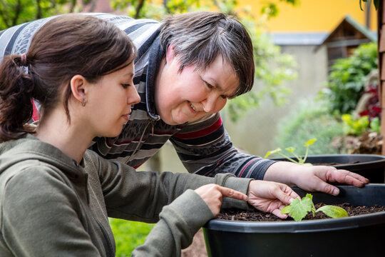 a caregiver explains to a mentally disabled woman how to plant zucchini in a bucket