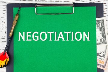 Obraz premium NEGOTIATION - word (text), a dart for darts and dollar bills on a green background of a notebook, a wooden white table. Business concept: buying, selling, commerce (copy space).