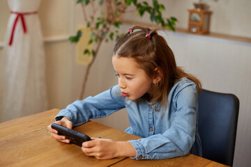 Happy kid girl playing game on mobile phone at home