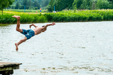 Teenagers jump into the water and swim in the lake on a hot summer day. Active recreation on an open pond. Children jump into the water and perform acrobatic tricks.