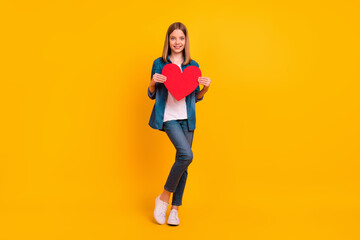 Fototapeta na wymiar Full body portrait of adorable cheerful girl hold large heart symbol card isolated on yellow color background