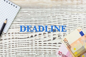 Naklejka premium DEADLINE - word (text) and euro money on a white wooden table, notebook, notepad. Business concept: buying, selling, commerce (copy space).