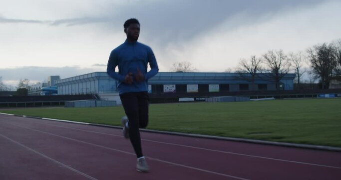 Young black runner jogging on empty running track with sky in the background.Blackmagic pocket 6k pro. Anamorphic