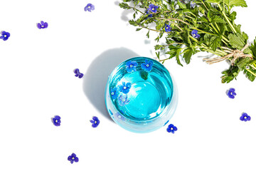 Cold tonic water and blue forget me not flowers bouquet on trendy stand isolated on white background