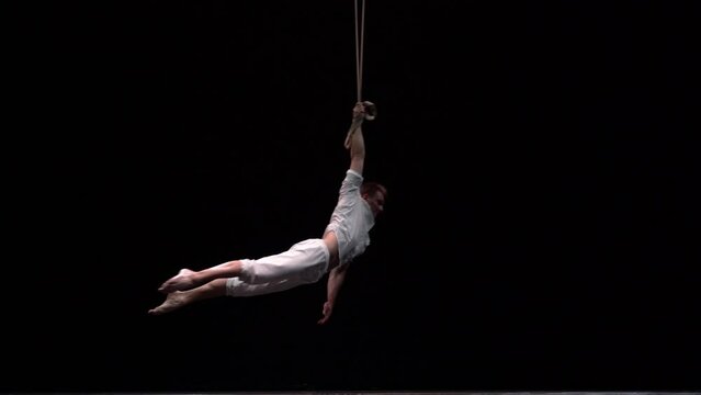 Muscular circus artist perform on the aerial straps on black background. Movement, strength concept
