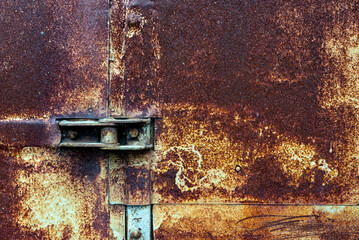 close-up photo of an old gate hinge on a door sheathed with rusty metal