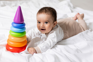 Fototapeta na wymiar cute little boy laying on blanket and playing with colorful pyramid toy , card, banner, health