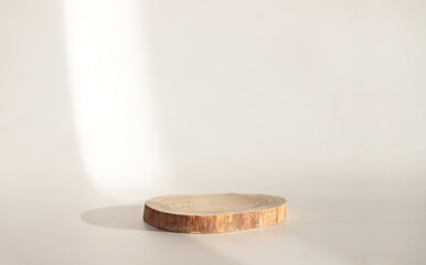 Wooden slab of round shape, podium for goods and cosmetics. Beige background with a sunbeam. Minimalism and trend