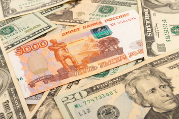 Russian national currency on top of US dollar banknote, top view of mixed rouble banknotes. Russian and American paper money. Rubles and US dollars exchange rate.