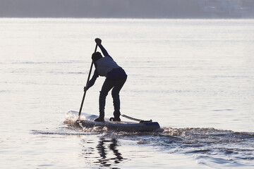 Silhouette of boy rowing on SUP (stand up paddle board) at dawn in the winter Danube river