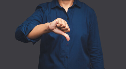 Negative concept. Close-up of businessman hand in a blue shirt showing thumbs down while standing on a gray background