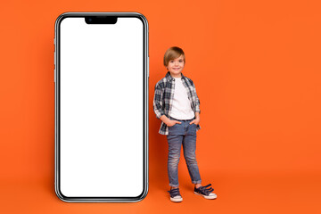 Full length photo of young boy confident promoter hands in pocket technology isolated over orange color background