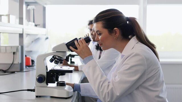 science research, work and people concept - female scientist with microscope working in laboratory