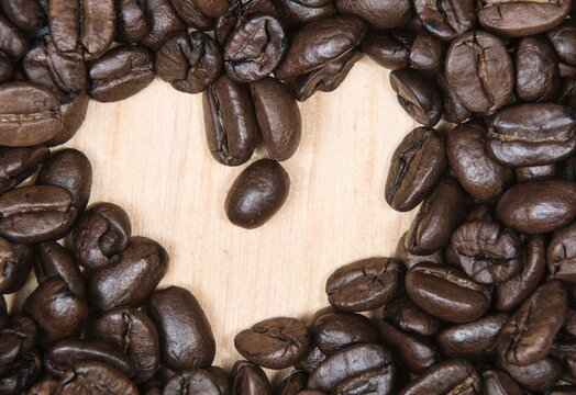 Wooden craft surface as a comfortable background wall or floor with different structures of light wood full of many coffee beans . A big heart sign shaped coffee beans. No people photography.