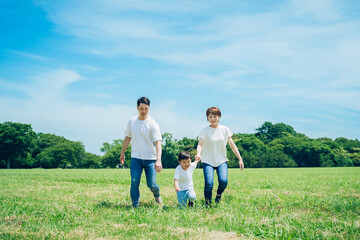 手を繋いで晴天の緑地を歩く親子3人