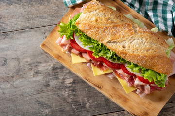 Submarine sandwich with ham, cheese, lettuce, tomatoes,onion, mortadella and sausage on wooden table	