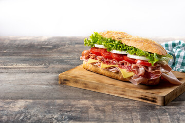Submarine sandwich with ham, cheese, lettuce, tomatoes,onion, mortadella and sausage on wooden table	