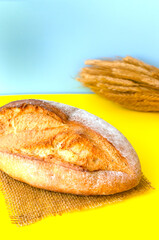 Fresh baked bread on a burlap with a bunch of wheat on a burlap on a yellow-blue background. Rustic style. The concept of Ukrainian bread, palyanytsya. Vertical orientation.
