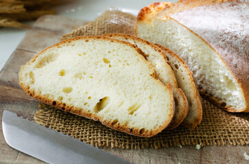 Slices of fresh baked bread on burlap with a knife on a light background. Rustic style. The concept of homemade bread. Horizontal orientation.