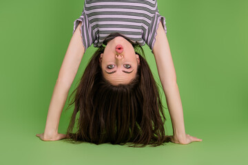 Upside down view portrait of attractive amazed girly funny girl standing on hands pout lips isolated over bright green color background © deagreez