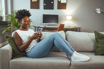 Shot of a young woman using a smartphone on the sofa at home. Woman using a cellphone while relaxing at home. Happy woman text messaging on smart phone at home..