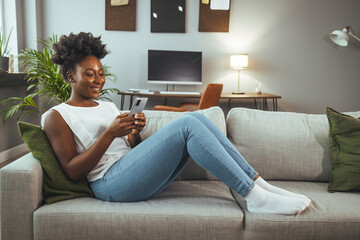 Obraz premium Shot of a young woman using a smartphone on the sofa at home. Woman using a cellphone while relaxing at home. Happy woman text messaging on smart phone at home..