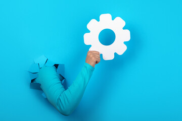 hand holding gear symbol over blue background