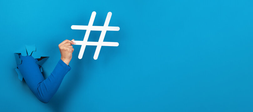 hand holding hashtag sign over blue background, social media concept, panoramic layout