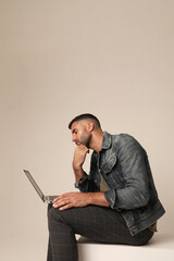 Bearded young man working with laptop while sitting indoor. Vertical mock-up.