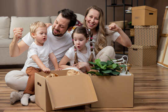 A cheerful family unpacks cardboard boxes after a move. The little girl and her brother take out the packed vases of pictures. Playing together while cleaning up.