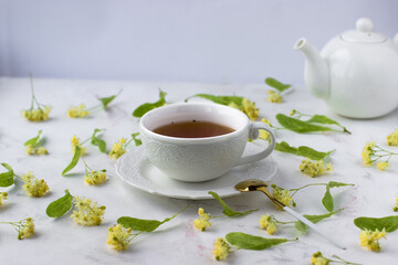 Tea with linden in a white cup on a white marble table. White teapot with aromatic tea