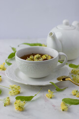 Tea with linden in a white cup on a white marble table. White teapot with aromatic tea