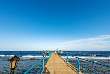 Obraz premium Seascape of the Red Sea near Marsa Alam, Egypt, Africa. Wooden pier above the coral reef used for diving, snorkeling and swimming with a group of tourists.