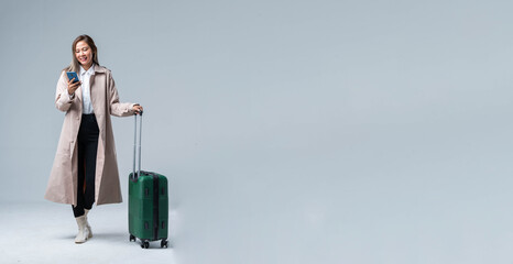 An asian smiling cheerful woman hand using smartphone credit card pull luggage bag prepare to new abroad journey travel studio shot on gray background