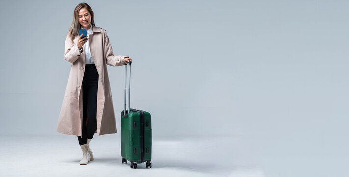 An asian smiling cheerful woman hand using smartphone credit card pull luggage bag prepare to new abroad journey travel studio shot on gray background