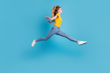 Fototapeta na wymiar Portrait of sportive active girl in motion jumping over in the air isolated on blue background having perfect stretching