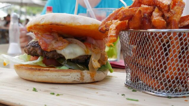 View on rench fries next to a huge cheeseburger or burger with a cutlet, lettuce, cheese and tomatoes inside. Unhealthy, fatty food on the street in a summer restaurant