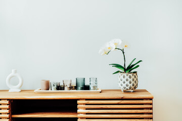 White orchid in blossom and tray with candles on the wooden cabinet against gray wall in modern...