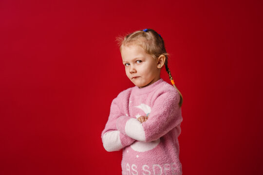 cute little Caucasian girl of 5 years old, insulted and offended on a red background. The baby is tired, capricious and turns away. Does not make contact. Close-up