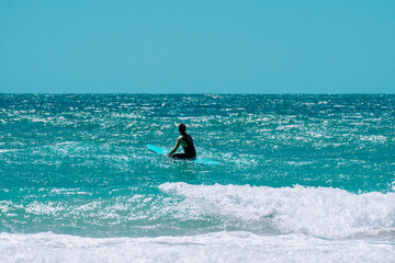 surfista en el agua la tabla de surf sentado en la playa mirando al horizonte