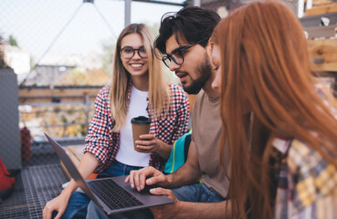 Group of diverse students brainstorming on university project while sitting at campus with laptop computer. Three friends learning together and discussing online information on netbook