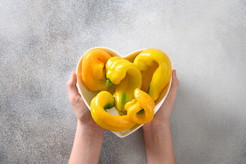 Ugly yellow pepper in white plate shaped of heart in child hands on gray background. Natural...