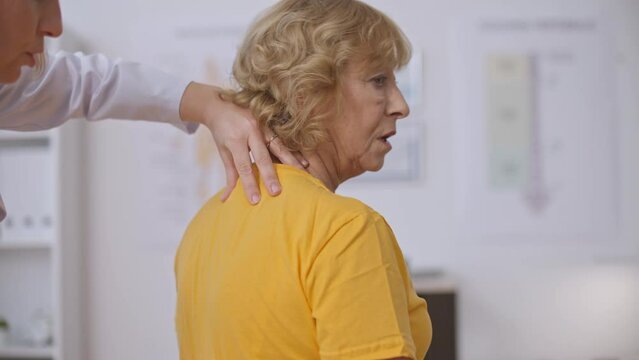 Unprofessional doctor examining senior woman's back, patient suffering pain