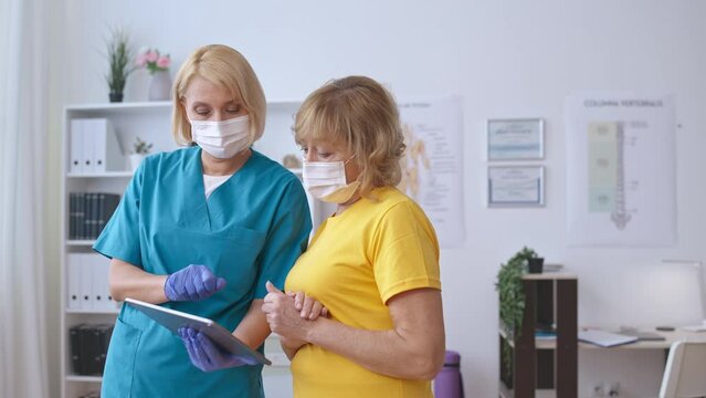 Medical specialist in face mask consulting patient, showing test results on tab