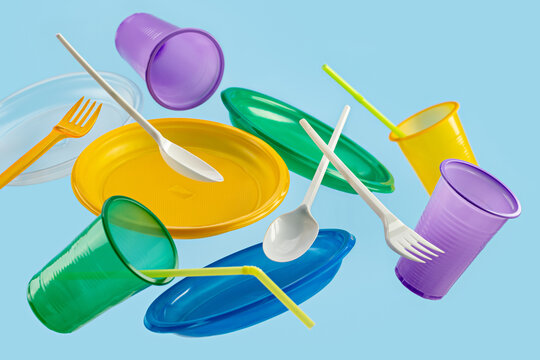 Flying multi-colored disposable plastic tableware on a blue background. The concept of ecology and recycling of plastic waste.