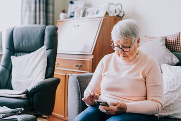 Senior woman using smartphone sitting on the sofa at home. Relaxed mature older lady holding mobile...
