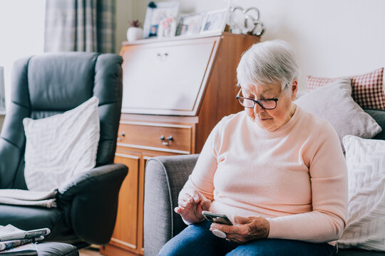 Senior woman using smartphone sitting on the sofa at home. Relaxed mature older lady holding mobile phone texting, buying online, playing games, checking apps on cellphone. Seniors and technology.