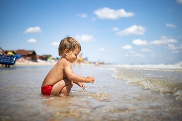 Fototapeta na wymiar Kid collects shells and pebbles in the sea on a sandy bottom under the summer sun on a vacation